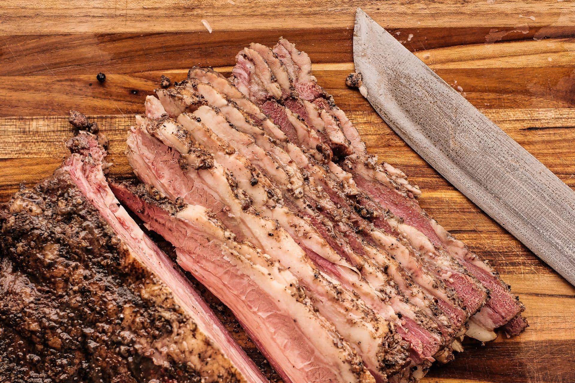 Aufgeschnittenes Brisket mit dunkler Bark und rosa Rauchring, Messer daneben auf Holzbrett