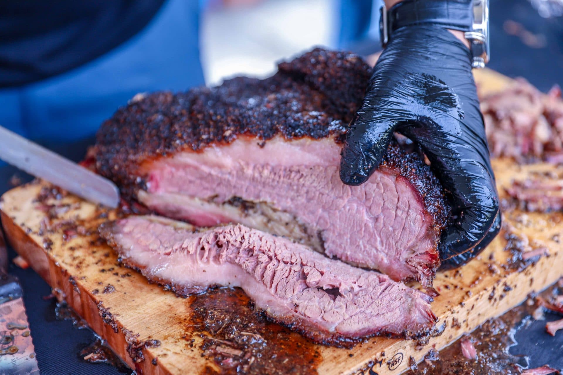 Brisket wird mit Handschuhen aufgeschnitten — dunkle Bark, rosa Rauchring